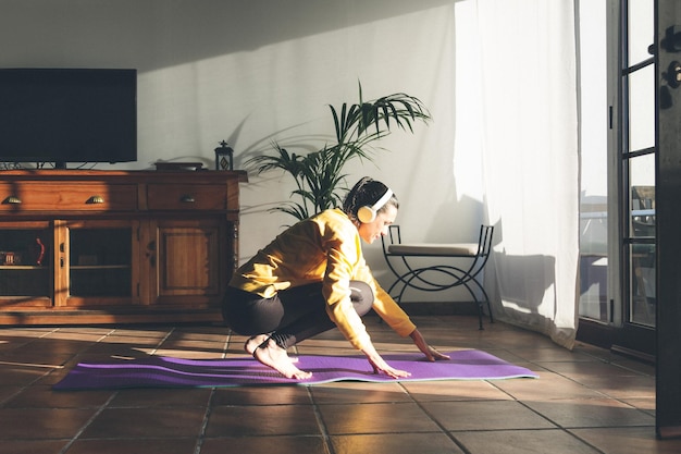 Une jeune femme brune caucasienne écoute de la musique pour pratiquer le yoga à la maison.
