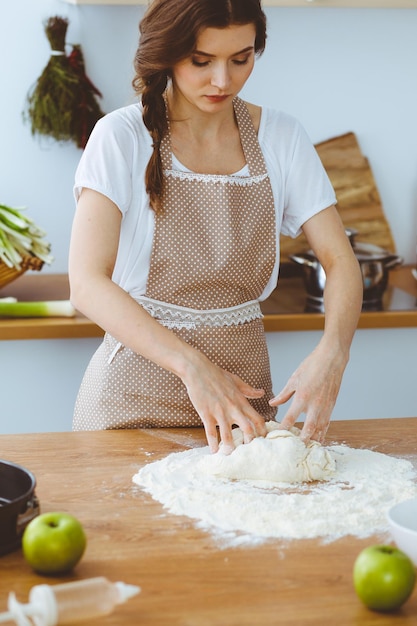 Jeune femme brune cuisinant de la pizza ou des pâtes faites à la main dans la cuisine. Maîtresse de maison préparant de la pâte sur une table en bois. Diète, nourriture et concept de santé.