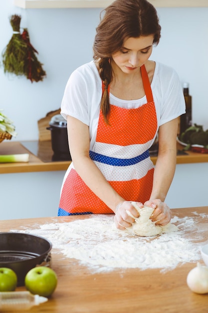 Jeune femme brune cuisinant des pizzas ou des pâtes faites à la main dans la cuisine. Femme au foyer préparant la pâte sur une table en bois. Concept de régime, de nourriture et de santé.