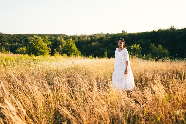 Jeune femme brune dans un champ sauvage Beauté naturelle et concept de romance Lumière du coucher du soleil Vue depuis l'arrière