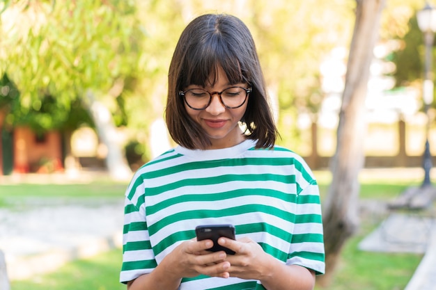 Jeune femme brune dans le parc à l'aide de téléphone portable