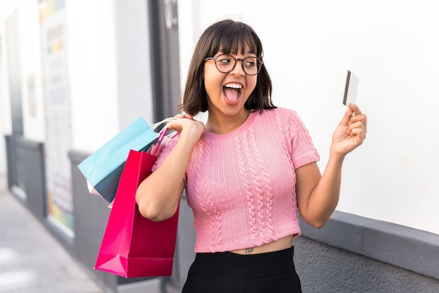 Jeune femme brune dans la ville tenant des sacs à provisions et une carte de crédit