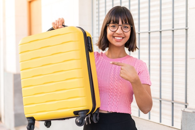 Jeune femme brune dans la ville en vacances avec valise de voyage