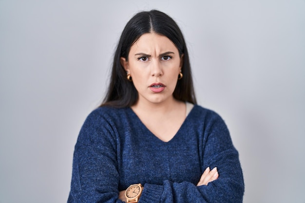 Jeune femme brune debout sur fond isolé expression désapprobatrice sceptique et nerveuse sur le visage avec les bras croisés personne négative