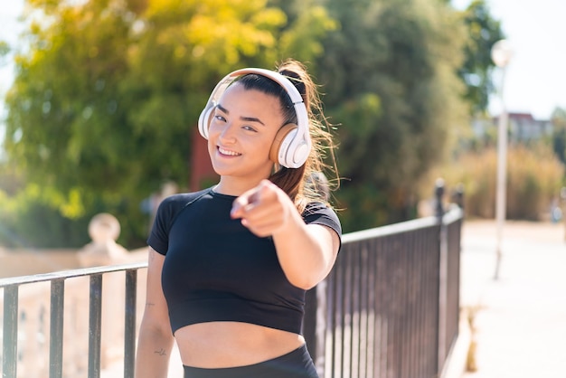 Une jeune femme brune écoute de la musique et pointe vers l'avant.