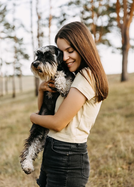 Une jeune femme brune embrasse un chien de race schnauzer en miniature et sourit.