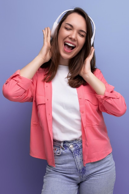 Une jeune femme brune énergique dans une chemise et un jean danse sur la musique d'un casque sans fil