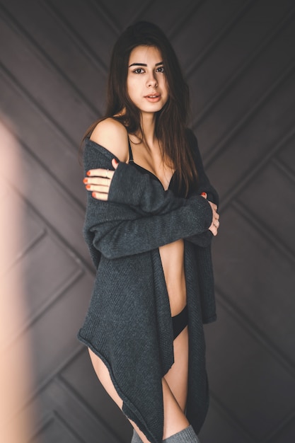 Jeune femme brune est enveloppée dans un cardigan gris sur un fond sombre monochrome