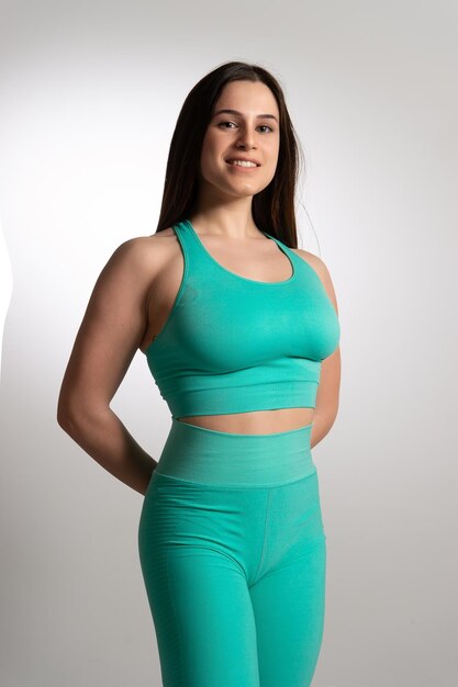 Jeune femme brune européenne souriante posant avec les mains derrière le dos Athlète féminine en vêtements de sport stretch turquoise isolé sur fond blanc Concept de mode de vie actif et sainxDxA