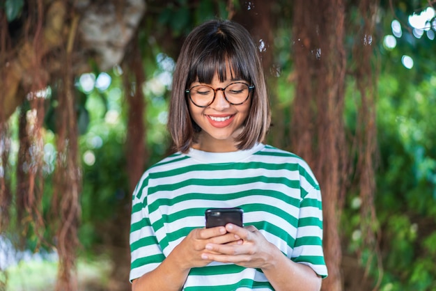 Jeune femme brune à l'extérieur dans un parc envoyant un message avec le mobile