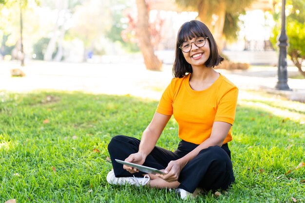 Jeune femme brune à l'extérieur tenant une tablette avec une expression heureuse