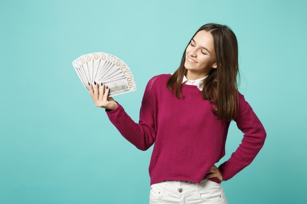 Jeune femme brune fille dans des vêtements décontractés posant isolé sur fond bleu portrait en studio. Concept de mode de vie des émotions des gens. Espace de copie maquette Tenir à la main un ventilateur d'argent liquide en billets en dollars