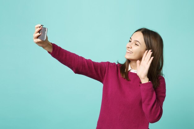 Jeune femme brune fille dans des vêtements décontractés posant isolé sur fond bleu portrait en studio. Concept de mode de vie des émotions sincères des gens. Maquette de l'espace de copie. souriant faisant selfie tourné sur téléphone portable