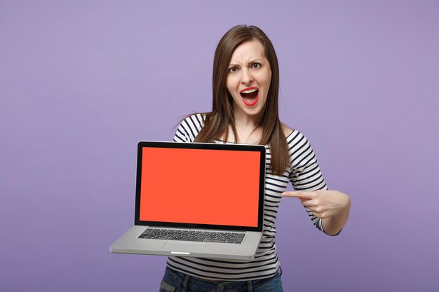 Jeune femme brune fille dans des vêtements rayés décontractés posant isolé sur fond violet violet portrait en studio. Concept de mode de vie des émotions sincères des gens. Maquette de l'espace de copie. Tenez l'ordinateur tablette pc.