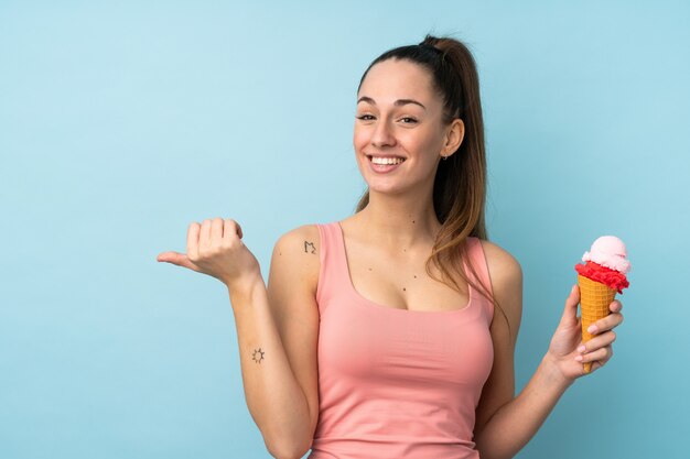 Jeune femme brune avec une glace au cornet sur un mur bleu isolé pointant vers le côté