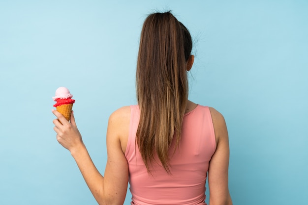 Jeune femme brune avec une glace au cornet sur un mur bleu isolé en position arrière