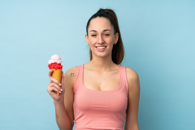 Jeune femme brune avec une glace au cornet sur un mur bleu isolé souriant beaucoup