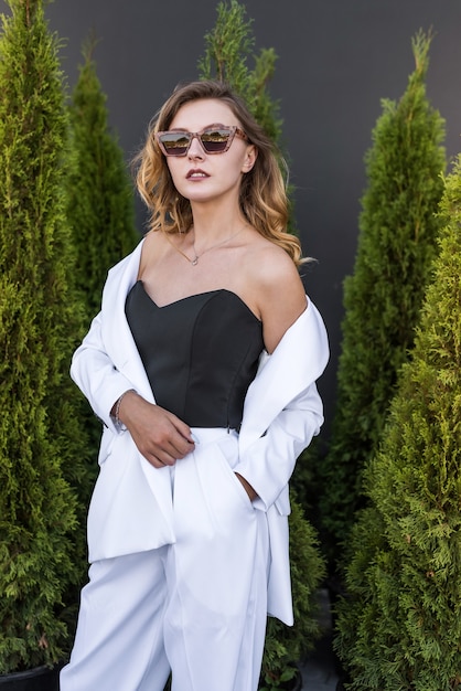 Jeune femme brune heureuse en costume blanc posant à la nature, cèdre blanc, heure d'été