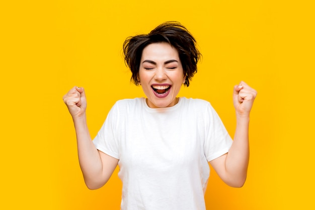 Jeune femme brune heureuse avec une coupe courte dans un T-shirt blanc sur fond jaune. portrait d'une jeune femme avec diverses émotions sur fond jaune. espace pour le texte