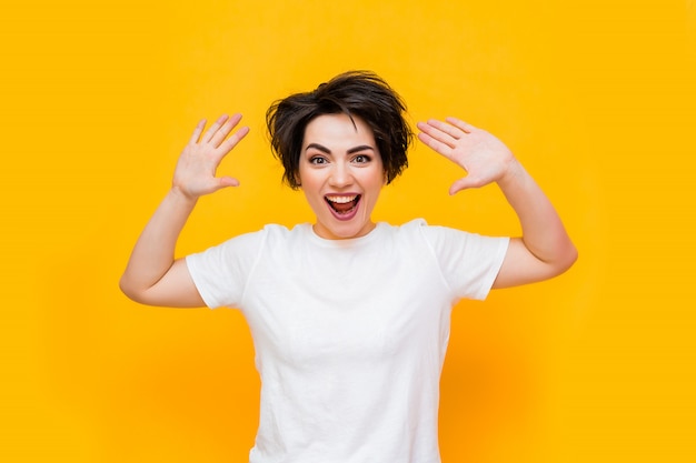 Jeune Femme Brune Heureuse Avec Une Coupe Courte Dans Un T-shirt Blanc Sur Fond Jaune. Portrait D'une Jeune Femme Avec Diverses émotions Sur Fond Jaune. Espace Pour Le Texte