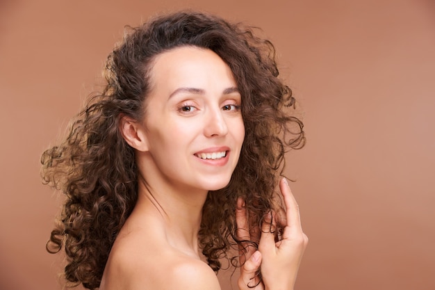 Jeune femme brune heureuse touchant de longs cheveux ondulés