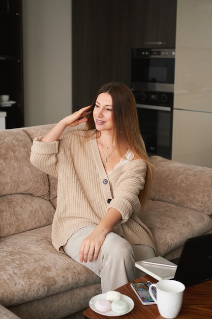 Jeune femme brune indépendante à la maison sur un canapé travaillant sur un ordinateur portable