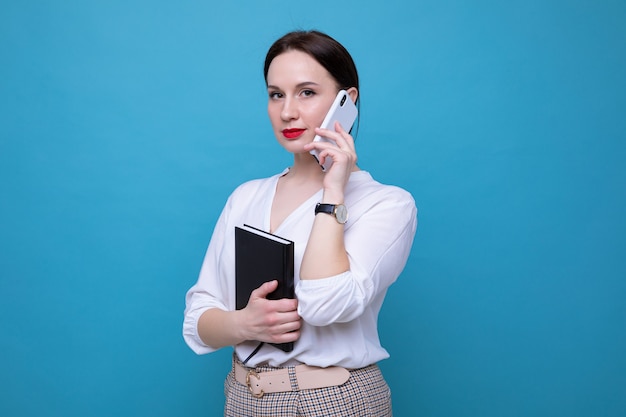 Une jeune femme brune avec un journal parle au téléphone sur un fond bleu