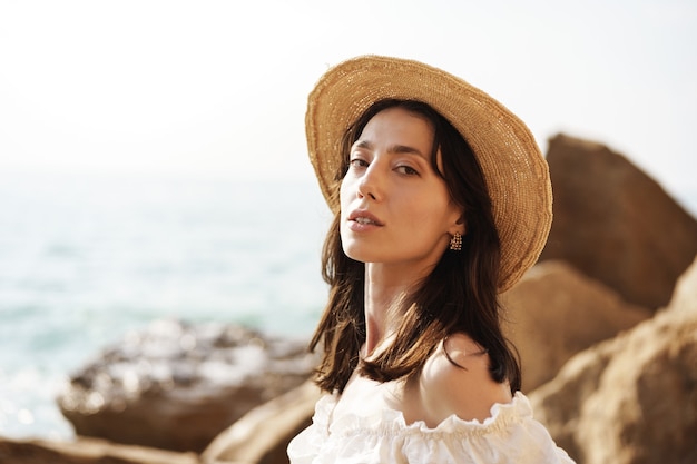 Jeune femme brune joyeuse posant contre la mer et les rochers