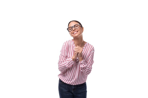 Jeune femme brune joyeuse et positive avec queue de cheval vêtue d'un chemisier rayé et d'un jean sur un