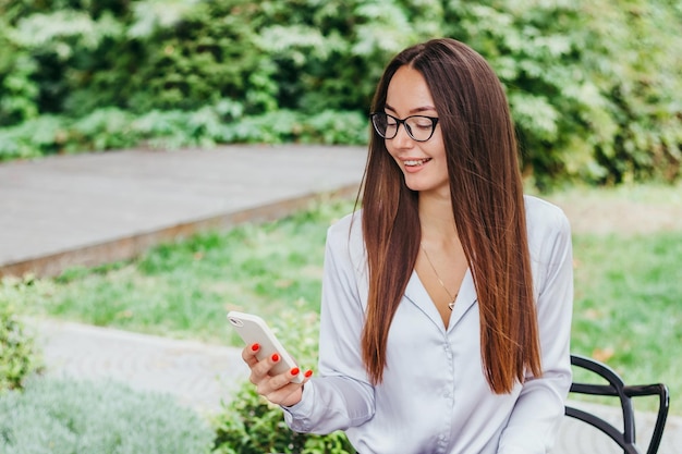 Une jeune femme brune à lunettes est assise à une table dans un café et travaille sur un ordinateur portable