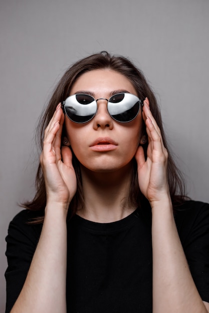 Jeune femme brune à lunettes noires et un t-shirt noir sur gris