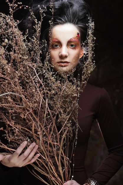 Jeune femme brune avec un maquillage lumineux avec des branches sèches