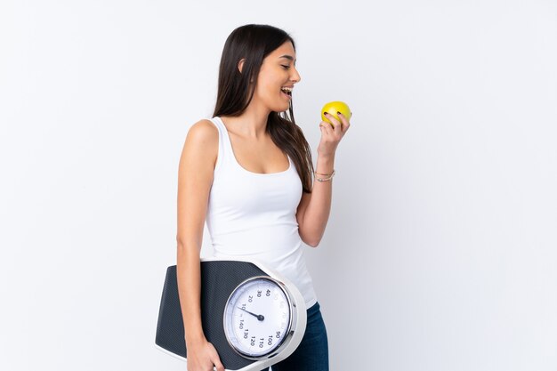 Jeune femme brune sur un mur blanc isolé avec machine de pesage et avec une pomme