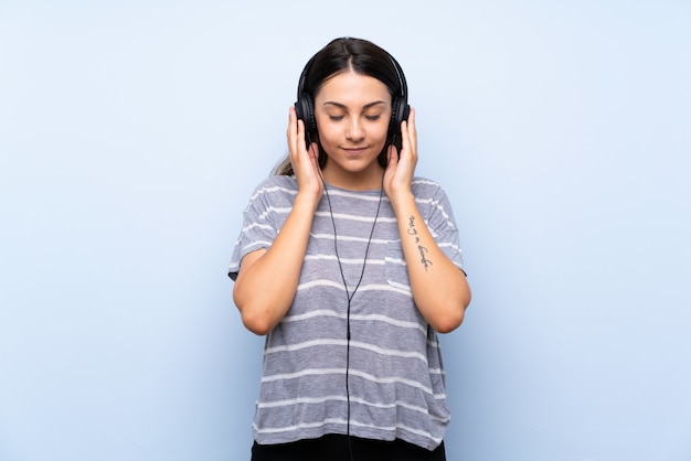 Jeune femme brune sur un mur bleu isolé, écouter de la musique avec des écouteurs