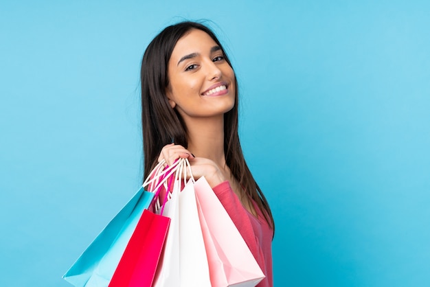 Jeune femme brune sur mur bleu isolé tenant des sacs à provisions et souriant