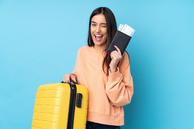 Jeune femme brune sur mur bleu isolé en vacances avec valise et passeport