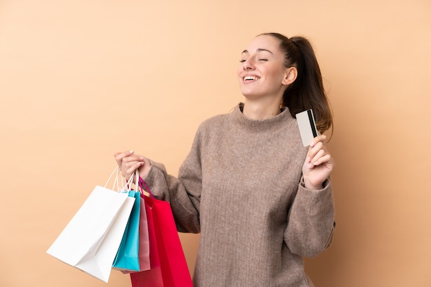 Jeune femme brune sur un mur isolé tenant des sacs à provisions et une carte de crédit