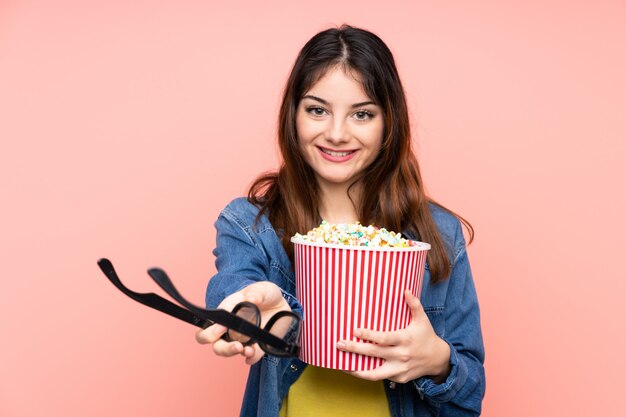 Jeune femme brune sur un mur rose avec des lunettes 3d et tenant un grand seau de pop-corn