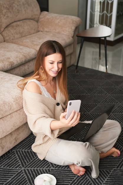 Jeune femme brune pigiste à la maison sur le canapé communique sur un smartphone