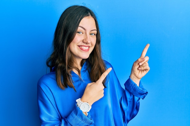 Jeune femme brune portant une chemise bleue décontractée souriant et regardant la caméra pointant avec deux mains et doigts sur le côté