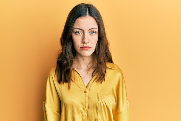 Jeune femme brune portant une chemise jaune décontractée avec une expression sérieuse sur le visage. simple et naturel en regardant la caméra.