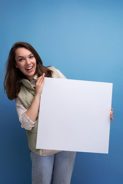 Jeune femme brune positive montrant une publicité sur une feuille blanche