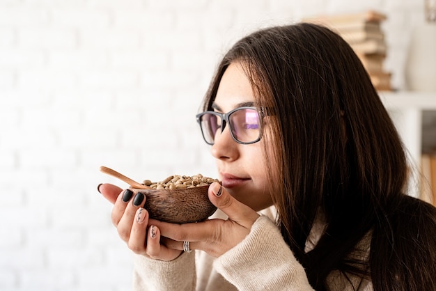 Jeune femme brune prépare du café dans une cafetière, sentant les grains de café vert