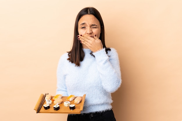 Jeune femme brune de race mixte tenant des sushis sur le mur couvrant la bouche avec les mains