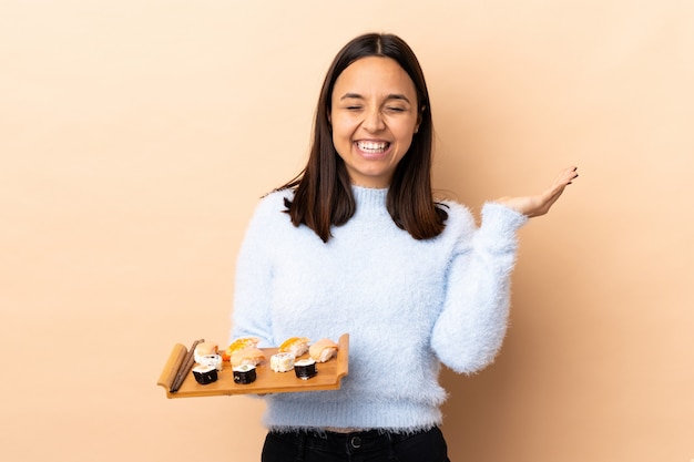 Jeune femme brune de race mixte tenant des sushis sur un mur isolé, souriant beaucoup