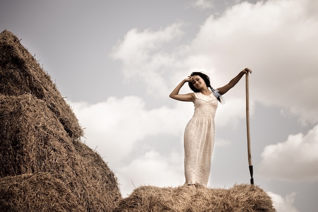 Jeune femme brune en robe blanche debout avec fourche à foin