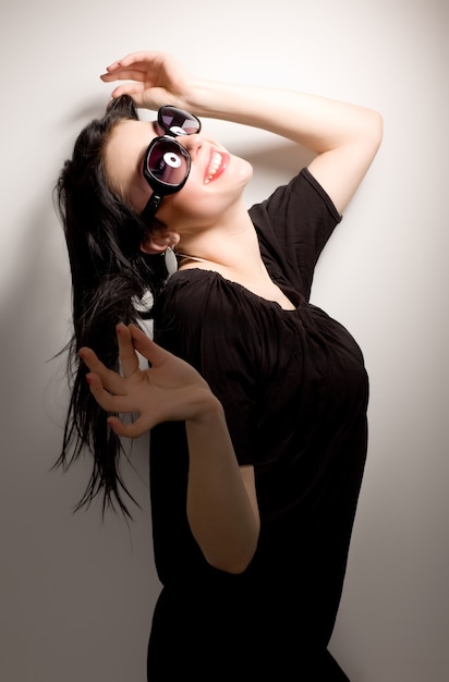 Jeune femme brune en robe noire et lunettes debout sur blanc