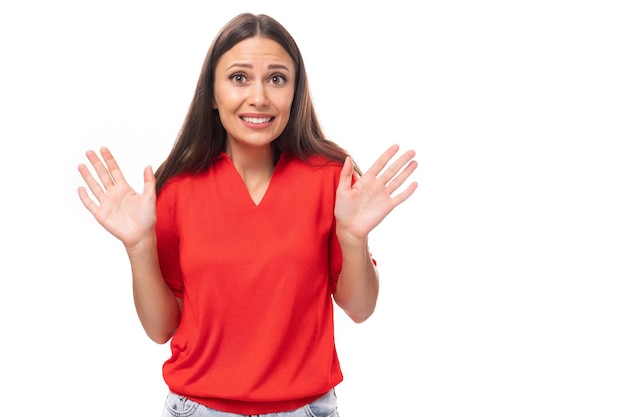 Jeune femme brune séduisante dans un chemisier vneck élégant rouge rempli ses bras de surprise