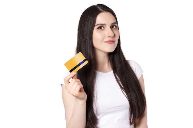 Jeune femme brune souriante caucasienne en t-shirt blanc tenant une carte de crédit bancaire en or pour une maquette