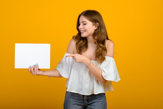 Jeune femme brune avec un sourire et de grands yeux surpris posant sur fond jaune.